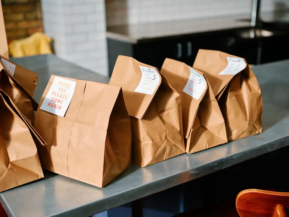 Several brown paper takeout bags with labels on a gray countertop.