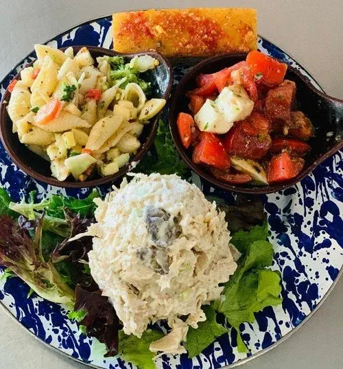 A plate with macaroni salad, beef stew with carrots and potatoes, potato wedge, and a side of mixed greens.